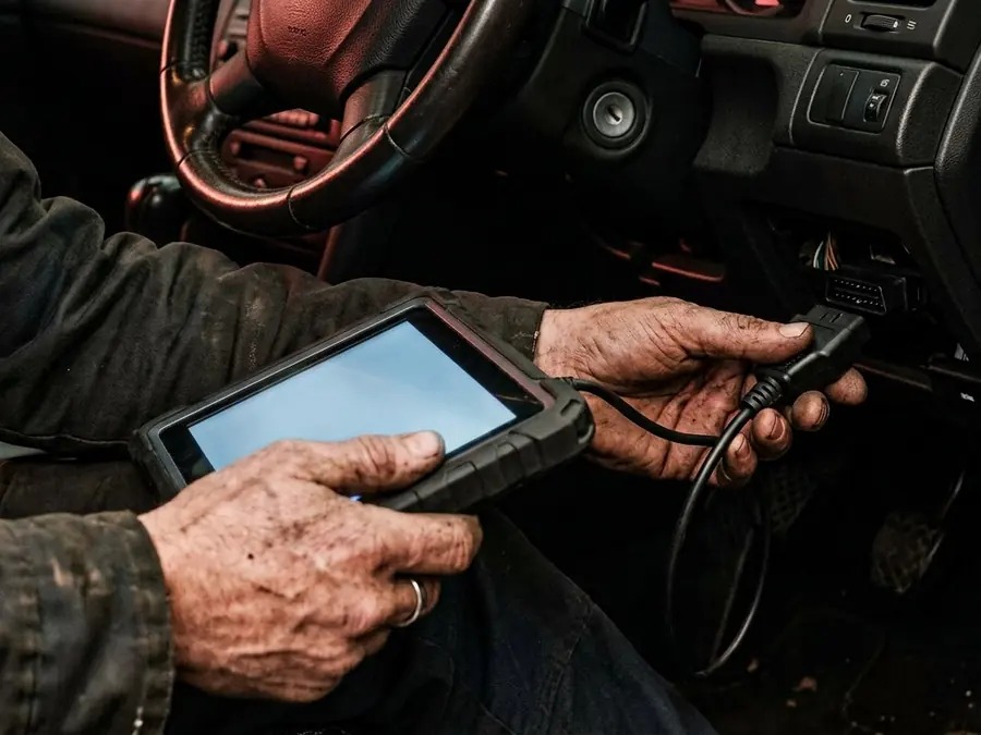 Technician using a diagnostic scanner connected to a car for vehicle fault diagnosis