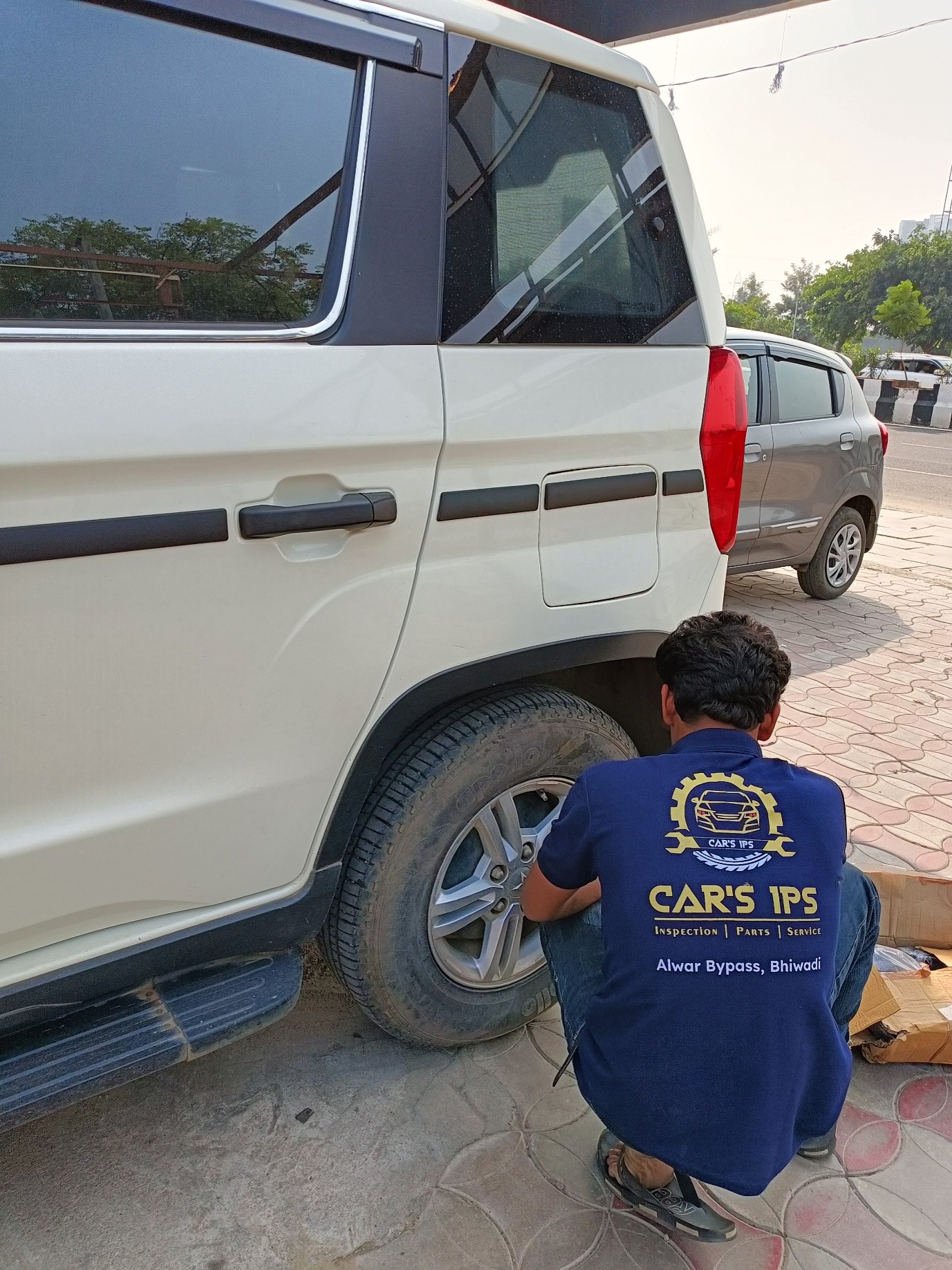 Car's IPS technician inspecting wheel and tyre of a white SUV outside the Bhiwadi workshop